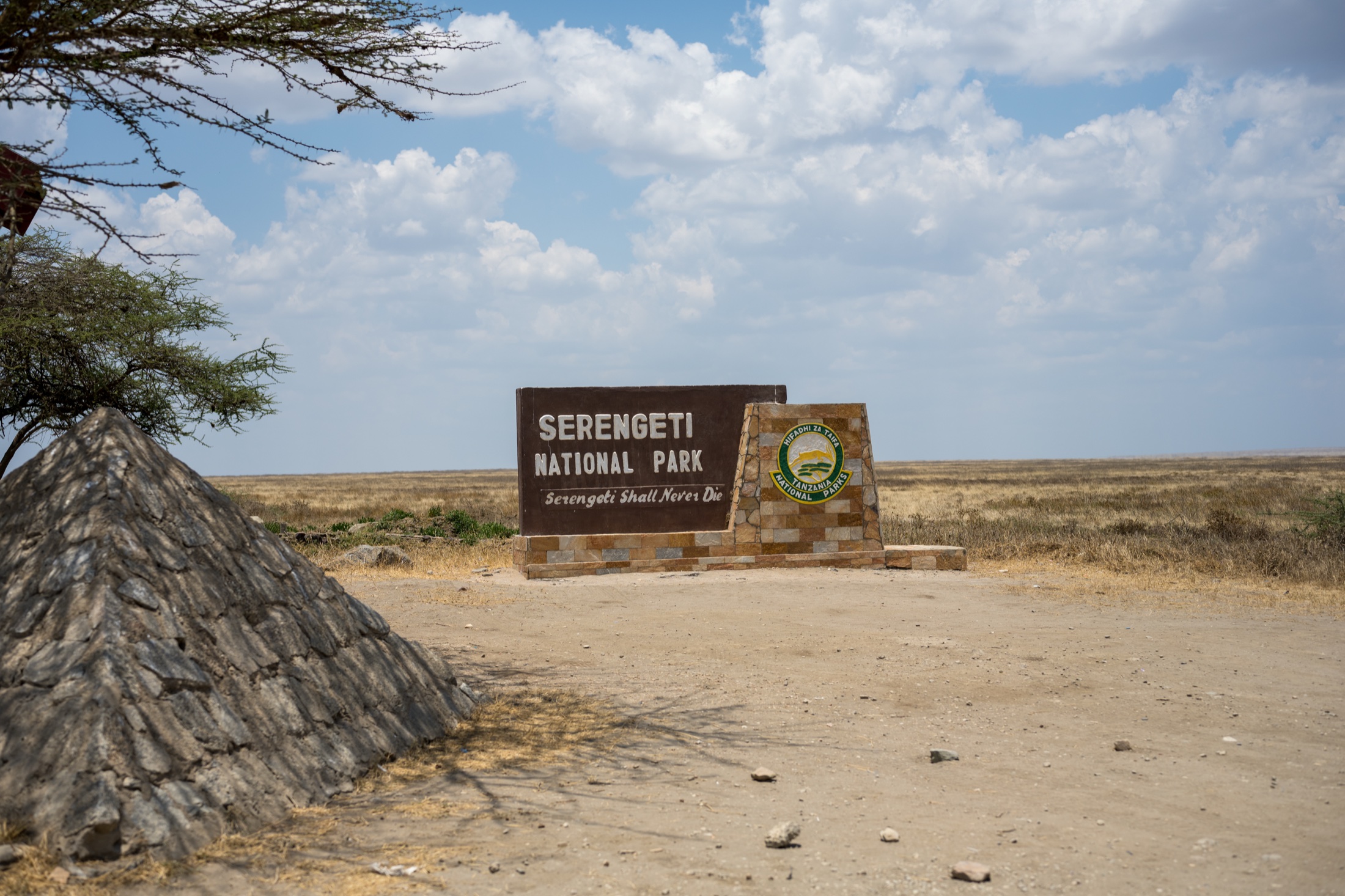 Eingangsschild des Serengeti-Nationalparks vor der weiten Ebene